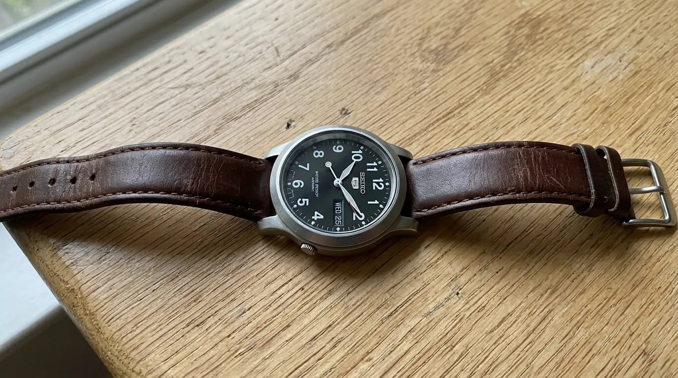 Casual phone photo of a Seiko wristwatch with brown leather strap lying on a plain wooden windowsill.